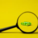 Lupa ao lado de um conjunto de comprimidos verdes sobre uma superfície amarela.