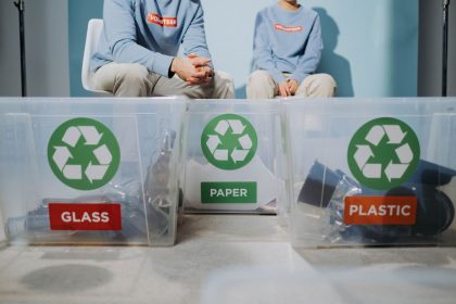 Pessoas organizam materiais recicláveis em recipientes separados para vidro, papel e plástico.