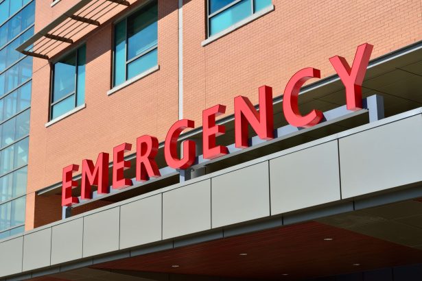 Entrada de um pronto-socorro hospitalar moderno, com acesso coberto e identificação em letras vermelhas.