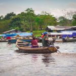 Homem e mulher navegam em uma pequena embarcação por um rio amazônico.