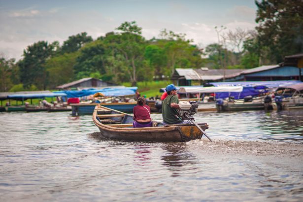 Homem e mulher navegam em uma pequena embarcação por um rio amazônico.